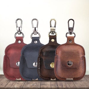 May include: Four leather Airpod cases with keychains in red, brown, black, and dark brown.