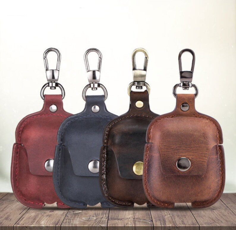 May include: Four leather Airpod cases with keychains in red, brown, black, and dark brown.