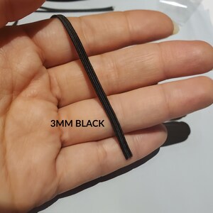 May include: A close-up of 3mm black elastic cord. The cord is held in a hand and the text "3MM BLACK" is visible below the cord.