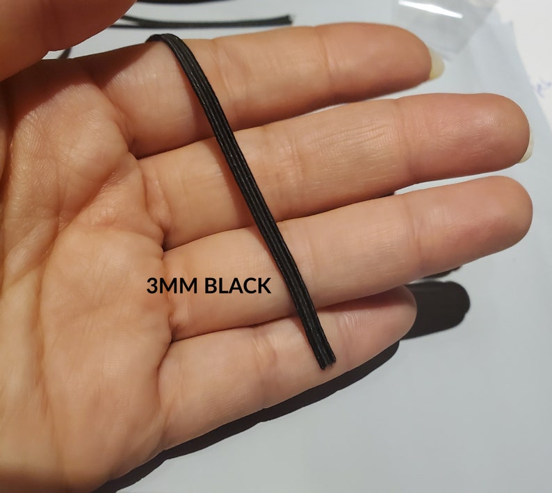 May include: A close-up of 3mm black elastic cord. The cord is held in a hand and the text "3MM BLACK" is visible below the cord.