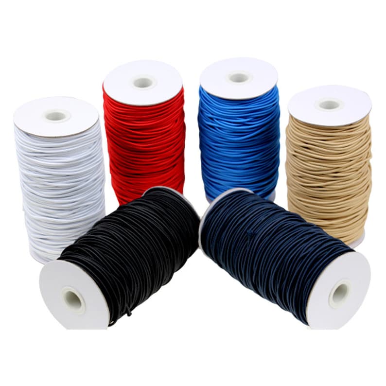 May include: Spools of elastic cord in various colors, including white, red, blue, tan, black, and navy. The cords are tightly wound on white cardboard spools, suitable for crafting and sewing projects.
