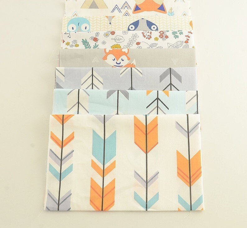 May include: A stack of eight fabric squares with different patterns. The patterns include arrows, foxes, and woodland animals. The fabrics are in shades of blue, orange, gray, and white.