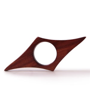 May include: A dark brown wooden bookmark with a rounded hole in the center. The bookmark is shaped like a pointed arrow.
