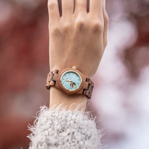 May include: A wooden wristwatch with a light blue face and gold accents. The watch has a brown wooden band.