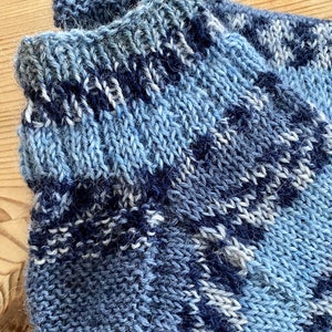 May include: Close-up of a blue and white striped knitted sock. The sock is made of a soft, fuzzy yarn.