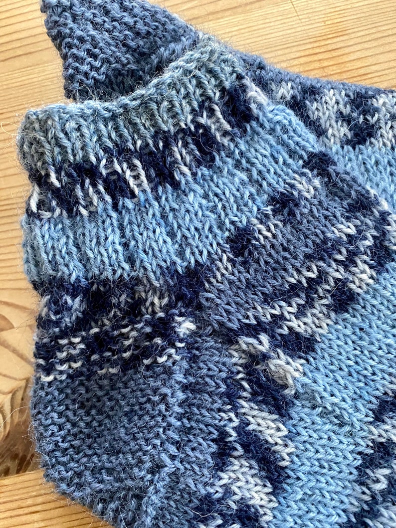 May include: Close-up of a blue and white striped knitted sock. The sock is made of a soft, fuzzy yarn.