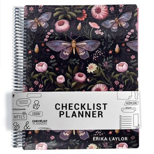 May include: A spiral-bound planner featuring a dark background with a pattern of pink flowers and butterflies. A white paper band wraps around the center with the text CHECKLIST PLANNER and ERIKA LAYLOR printed on the cover.