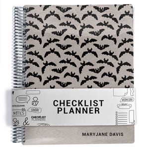 May include: A spiral-bound planner with a tan cover featuring a repeating black bat pattern. A white paper band wraps around the center, printed with the text CHECKLIST PLANNER, CHECKLIST PLANNERS, and various hand-drawn icons. The name MARYJANE DAVIS is printed in black on the bottom right.