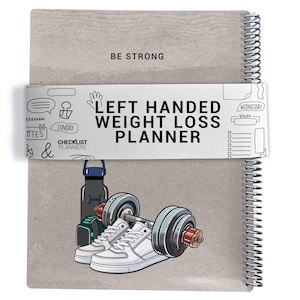 May include: A grey spiral-bound planner with the words "BE STRONG" at the top. A white band wraps around the planner with the text "LEFT HANDED WEIGHT LOSS PLANNER". The planner features illustrations of a water bottle, trainers, a smartwatch, and a barbell.