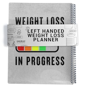 May include: A grey spiral-bound weight loss planner. The cover reads "WEIGHT LOSS" and "IN PROGRESS." A white band across the centre says "LEFT HANDED WEIGHT LOSS PLANNER" with small icons. The planner has a progress bar with red, orange, yellow, and green sections.