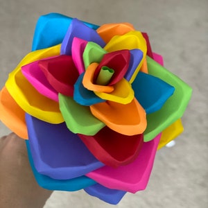 May include: A colorful paper flower with layers of blue, purple, pink, red, orange, yellow, green, and light green.