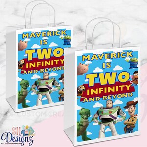 May include: Two white paper gift bags featuring a blue sky background with white clouds and Toy Story characters including Buzz Lightyear, Rex, and Hamm. The text reads MAVERICK IS TWO INFINITY AND BEYOND in yellow, red, and blue lettering.