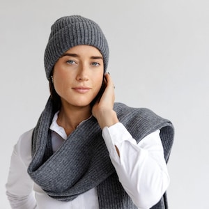 以下が含まれることがあります： グレーのリブ編みニット帽とスカーフのセット。帽子は頭の上にあり、スカーフは首にかけられています。このセットは柔らかく暖かい素材でできており、寒い季節に最適です。白いボタンダウンシャツを着ています。