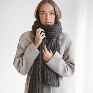以下が含まれることがあります： グレーのコートを着て、首に濃いグレーのニットのストールを巻いた女性
