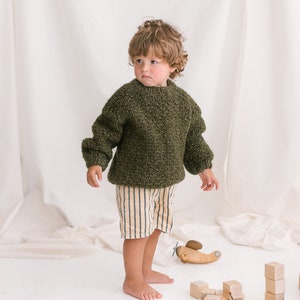 May include: A young child wearing a green knitted sweater and striped pants plays with wooden toys, including a helicopter and building blocks.