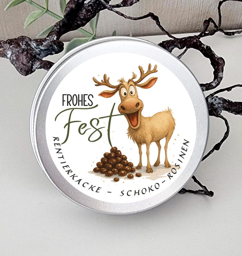 May include: A round silver metal tin featuring a cartoon reindeer with large eyes and antlers, a pile of brown chocolate-covered raisins, and the text "FROHES FEST RENTIERKACKE - SCHOKO - ROSINEN" printed in black and green lettering.