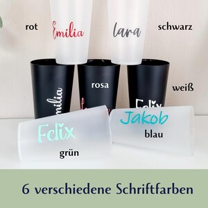 May include: A collection of personalized cups in various colors. The cups are white and black, with names written in red, black, and blue. The text "6 verschiedene Schriftfarben" is at the bottom.