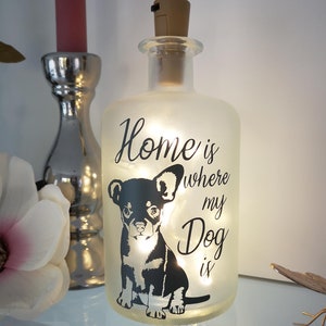 Könnte beinhalten: Eine gefrostete Glasflasche mit einem Korkverschluss und einem Licht im Inneren. Die Flasche hat eine schwarze Silhouette eines Hundes und den Text "Home is where my Dog is".