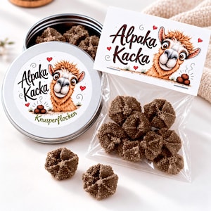 May include: A round silver metal tin and a clear plastic bag containing brown textured food pieces. Both feature a label with a cartoon alpaca and the text Alpaka Kacka. The tin lid also includes the text Knusperflocken.