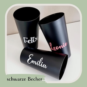May include: Three black cylindrical tumblers with personalized names in white and pink. The names "Felix", "Leonie", and "Emilia" are displayed on the tumblers. The phrase "schwarze Becher" is at the bottom.