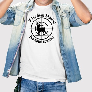 以下が含まれることがあります： 黒い鹿のクロスヘアースコープのグラフィックが描かれた白いTシャツ。グラフィックの周りのテキストは「If I've Gone Missing I've Gone Hunting.」です。