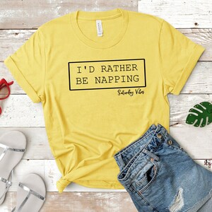 May include: Yellow t-shirt with black text that reads "I'd rather be napping Saturday Vibes".