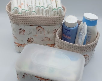 May include: Three white fabric baskets with a woodland animal print. The baskets are filled with baby supplies, including diapers, wipes, and lotion. The lotion bottle is blue and white and says "Babylove" on the label.