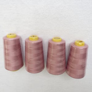 Könnte beinhalten: Vier Spulen mit rosafarbenem Garn und gelben Plastikkappen.