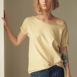 Peut inclure: Un t-shirt jaune pâle à épaules dénudées avec des manches retroussées. Le t-shirt est fait d'un tissu doux et confortable et a une coupe décontractée.