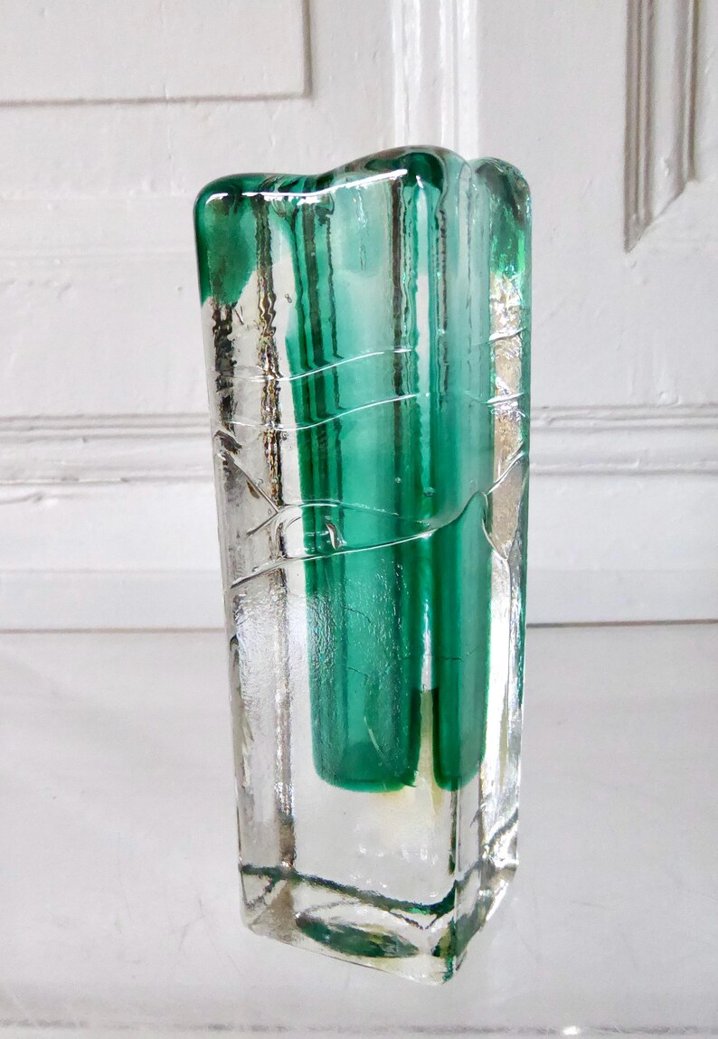 May include: A rectangular glass vase with a clear exterior and a vibrant green interior. The vase has a textured, cracked appearance on the outside, with vertical green stripes visible through the clear glass. The vase is a decorative item.