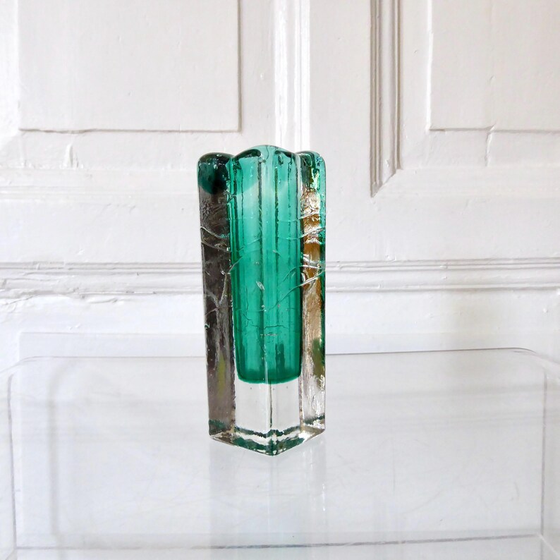May include: A rectangular, clear glass vase with a teal-colored interior. The vase has a textured, cracked appearance on the exterior, with a scalloped top edge. The vase is displayed on a clear surface against a white background.
