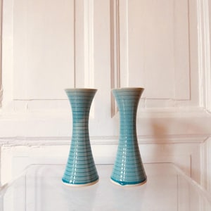 Könnte beinhalten: Zwei türkisfarbene Vasen mit horizontalen Streifenmustern. Die Vasen haben eine ausgestellte Ober- und Unterseite mit einem schmaleren Mittelteil. Der Hintergrund ist eine weiße Tür.