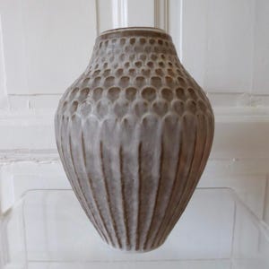 Peut inclure: Un vase en céramique gris texturé. La partie supérieure présente un motif en nid d'abeille, tandis que la partie inférieure est ornée de rainures verticales. Ce vase de couleur neutre convient à divers styles de décoration intérieure.