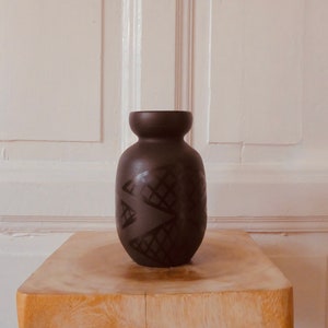 Puede incluir: Un jarrón de cerámica negro con un patrón geométrico. El jarrón tiene un cuerpo redondeado y una boca ancha.