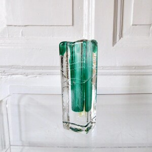 May include: A rectangular glass vase with a clear exterior and a vibrant green interior. The vase has a textured surface with a wavy top edge. The interior green glass is visible through the clear glass, creating a striking contrast. A decorative home decor item.