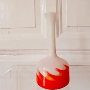 May include: A decorative glass vase with a rounded base and a long, slender neck. The vase has a striking design, with a red base that blends into white, resembling flames. The vase is approximately 30 cm tall.