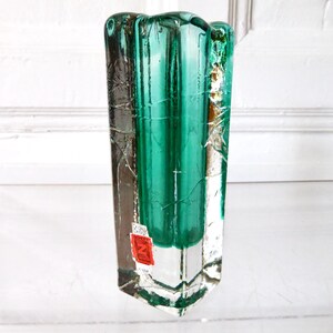 May include: A rectangular, clear glass vase with a teal-green interior. The vase has a textured, cracked appearance on the exterior. A red and white sticker is affixed to the front. The vase is approximately 10 inches tall.