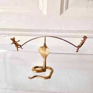 Può includere: Scultura in ottone raffigurante un cobra con una barra curva in equilibrio sulla testa. Due piccole figure sono attaccate alla barra, creando un design stravagante ed equilibrato. Estetica vintage.