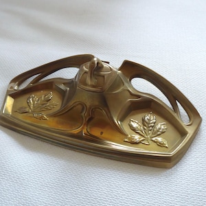 Op de afbeelding: Antieke messing bureauset met een bladeren design. De set bevat een penhouder en een inktpot, met Art Nouveau-stijl. Het messing heeft een warme, verouderde patina, en het ontwerp omvat gebogen lijnen en organische vormen.