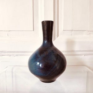 Könnte beinhalten: Eine Keramikvase mit bauchigem Körper und engem Hals, die eine glänzende Glasur in tiefen Blau-, Schwarz- und Brauntönen aufweist, mit subtilen wirbelnden Mustern auf der gesamten Oberfläche, aufrecht stehend mit einer glatten, runden Form.