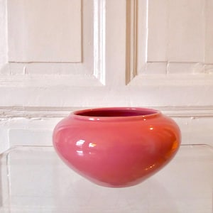 May include: A spherical, pink ceramic bowl with a wide opening. The bowl has a smooth, curved form and a vibrant, solid colour. The interior of the bowl is a darker shade of pink.