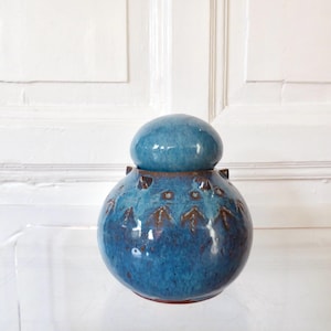 Peut inclure: Un pot en céramique bleu avec un couvercle assorti. Le pot a un corps rond avec un motif texturé et de petites poignées. Le couvercle est de forme arrondie. Le pot mesure environ 15 cm de haut.