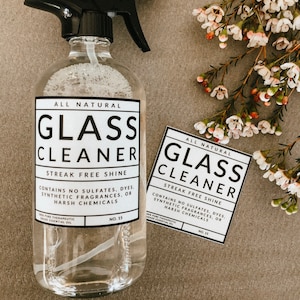 Può includere: Flacone spray in vetro trasparente con ugello nero ed etichetta bianca con la scritta "All Natural Glass Cleaner, Streak Free Shine". Un'etichetta abbinata è accanto al flacone. L'immagine include anche fiori bianchi e rosa.