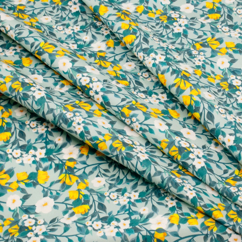 May include: A fabric with a floral pattern featuring white flowers and yellow buds on a teal background.