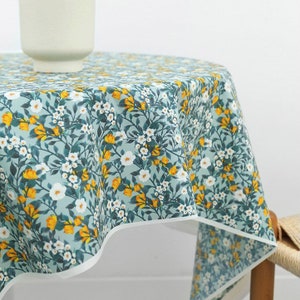 May include: A round tablecloth with a floral pattern in shades of blue, white, and yellow. The tablecloth has a white border and is made of a soft, cotton fabric.