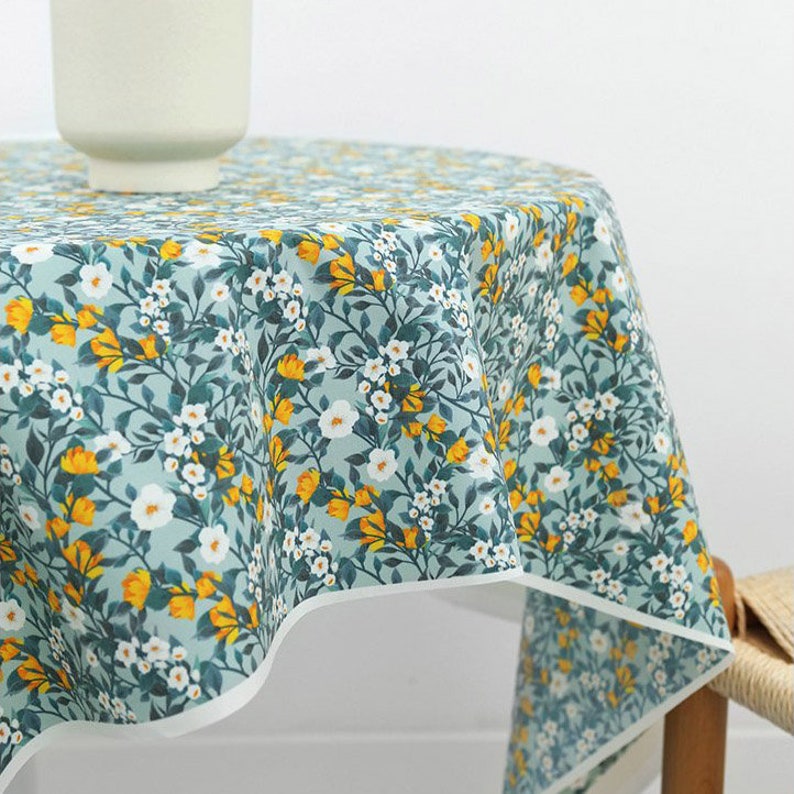 May include: A round tablecloth with a floral pattern in shades of blue, white, and yellow. The tablecloth has a white border and is made of a soft, cotton fabric.