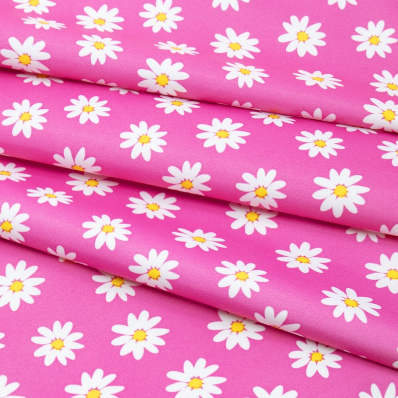 May include: Pink fabric with a white daisy pattern. The fabric is folded in layers, creating a textured effect.