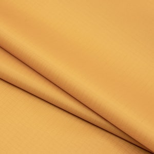 May include: A close-up of a smooth, golden yellow fabric. The fabric is folded in half, showing the texture and colour.