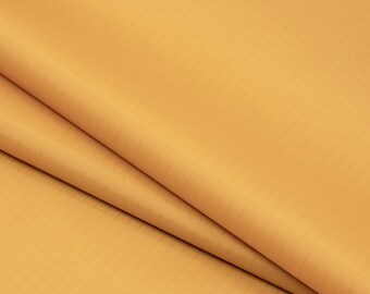 May include: A close-up of a smooth, golden yellow fabric. The fabric is folded in half, showing the texture and color.