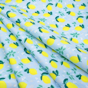 May include: A light blue fabric with a repeating pattern of yellow lemons and white flowers. The fabric is folded in half, showing the pattern on both sides.
